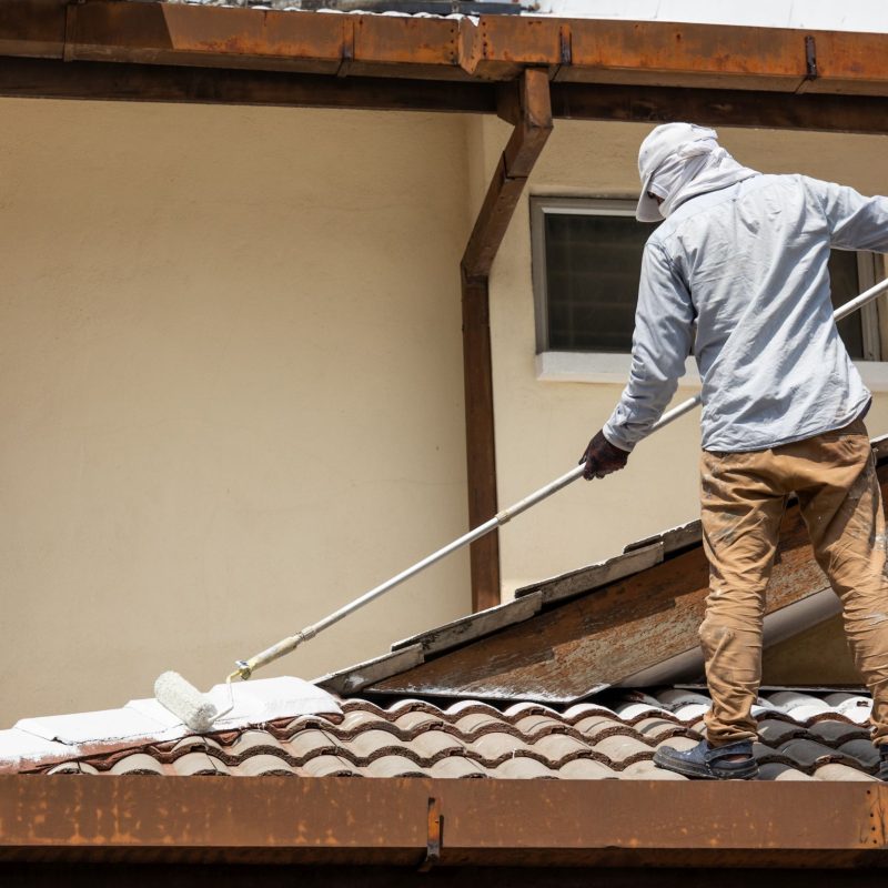 Worker adding undercoat foundation paint onto rooftop with roller as primer at residential building in renovation